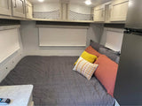 Inviting RV rental bedroom: bed with grey comforter & colorful pillows, overhead cabinets, and window blinds.