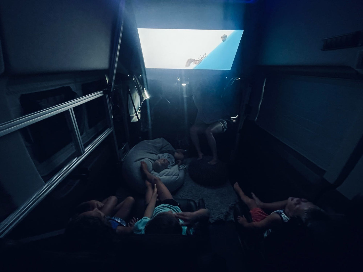 Fun family movie night inside an RV rental! Kids are cozy, watching an animated film projected on the wall.