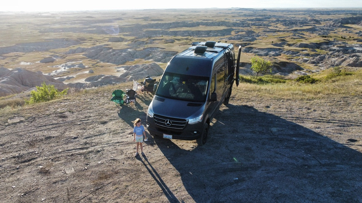 Experience stunning views with an RV rental! This camper van is parked overlooking badlands, with a child enjoying the vast landscape.