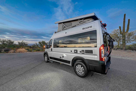 Silver RV rental camper van with pop-top in desert landscape with saguaro cactus at dusk. Perfect for road trips.