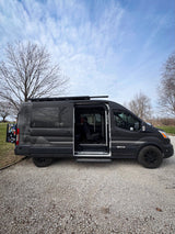 Explore with this dark grey Flatlander vandoit rv rental van on gravel, side door open. Perfect for van life adventures.