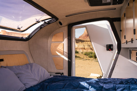 Cozy RV rental bedroom interior with a large window showcasing desert views. Features a bed, skylight, and storage.