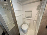 An RV rental wet bath, showing the white toilet, shower head, and small shelf. Ideal for compact living on the road.