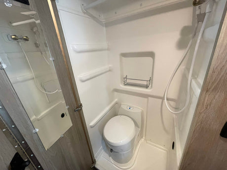 An RV rental wet bath, showing the white toilet, shower head, and small shelf. Ideal for compact living on the road.