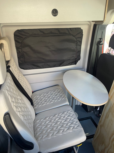 This RV rental features comfortable quilted seating, a round dining table, and a window cover for privacy.