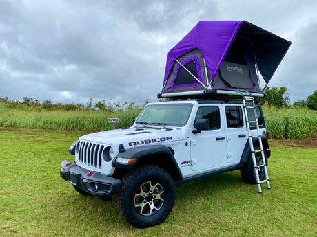 Explore with this white Jeep Wrangler RV rental featuring a vibrant purple rooftop tent, perfect for outdoor camping.