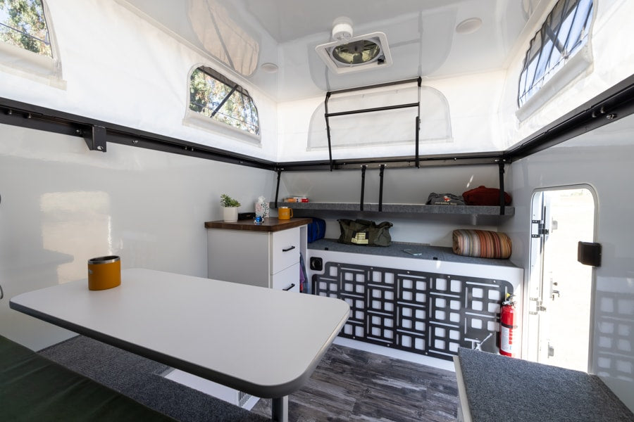 This clean RV rental interior features a dining table, organized storage, and bright pop-up windows for comfortable mobile living. — photo 6