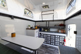 This clean RV rental interior features a dining table, organized storage, and bright pop-up windows for comfortable mobile living.