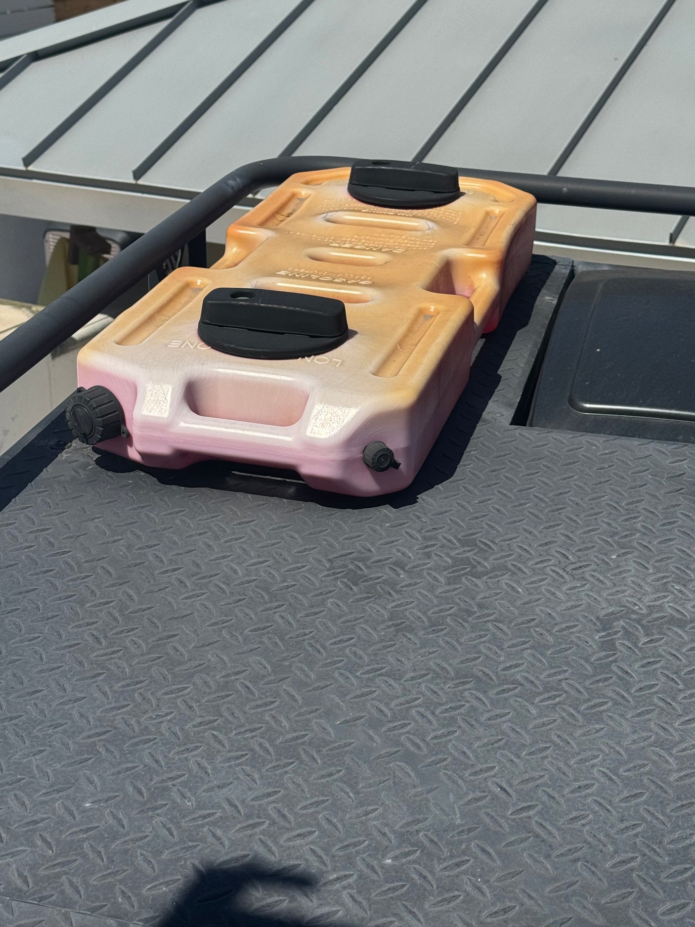 Discolored gasoline RotopaX container on an RV rental vehicle, secured to a textured diamond plate roof. Road trip ready.