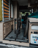 An RV rental interior with a mountain bike neatly stored for transport, featuring custom cabinetry, bed, and utility connections.
