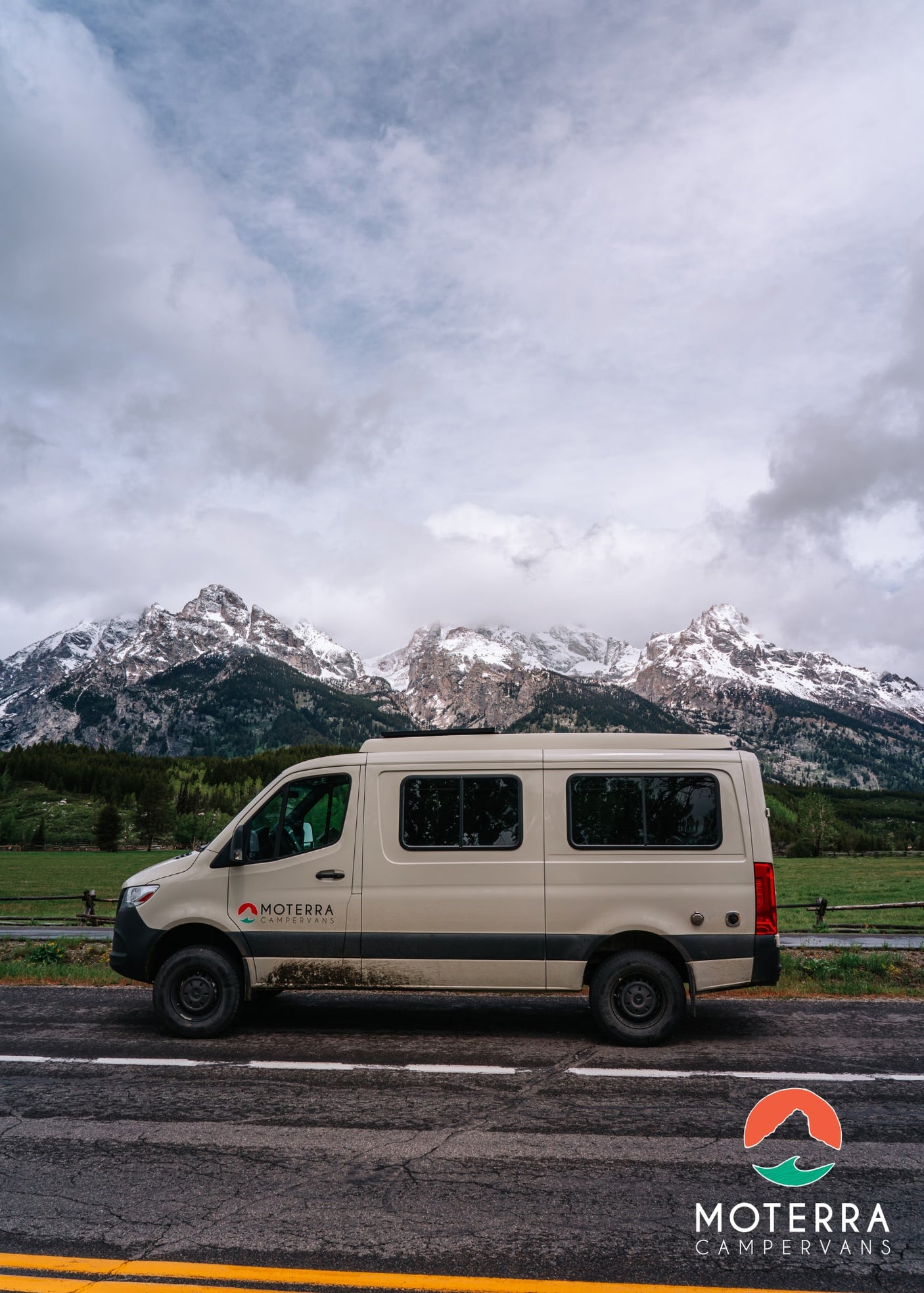 Beige Moterra RV rental campervan on a road, with majestic snow-capped mountains and green forests in the background.