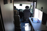 Camper van interior for RV rental. Shows front cabin with dashboard, seats, and a modern digital control panel.