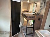 Compact RV rental interior with bunk beds, small sink, and a door. Perfect for maximizing space on the go.