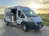 Silver Ram ProMaster camper van for rv rental, door open to interior, parked by a field at sunset.