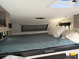 RV rental interior featuring a comfy bed with "FISHHOOK" detail on the frame, storage nets, and a skylight.