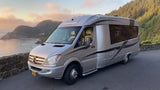 Scenic Oregon coast rv rental parked overlooking the Pacific Ocean at sunset, with a distant lighthouse visible.