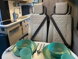 Inside an rv rental: compact kitchen, dining table set with green dinnerware for two, and comfortable passenger seats.