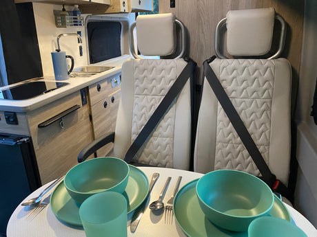 Inside an rv rental: compact kitchen, dining table set with green dinnerware for two, and comfortable passenger seats.