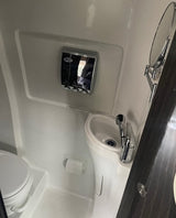 Compact RV rental bathroom features a toilet, sink, wall-mounted dispenser, and extendable mirror.