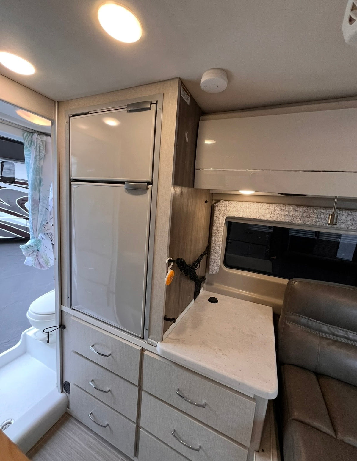 This RV rental shows a compact interior with a fridge/freezer, drawers, and counter, beside a wet bath with a curtain. — photo 8