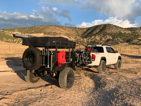 White Toyota Tacoma towing an off-road overlanding trailer with a rooftop tent & bikes – ideal for an RV rental adventure.
