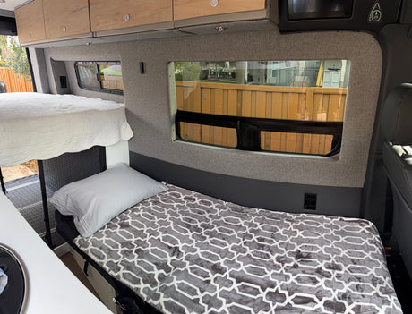 Cozy RV rental interior with bunk beds, wooden cabinets, and windows offering outdoor views. Perfect for camper van adventures.