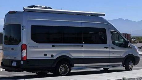 A silver Ford Transit camper van, ideal for RV rental. Equipped with an awning for your travels.
