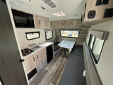 Interior of an RV rental showing a compact kitchenette with stove, sink, microwave, plus a dining area with bench seating.