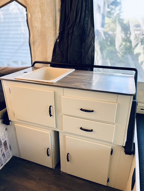 Discover this RV rental's renovated kitchenette: a bright sink, cream cabinets, and wood-look floors await your next trip.