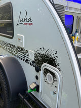 Close-up of a Luna Rover teardrop rv rental with black splatter graphics, power hookup, and open kitchen hatch.