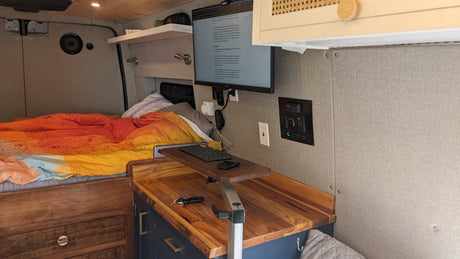 Well-equipped RV rental van interior: bed, monitor workspace, and climate controls for remote work and travel.