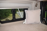 RV rental interior: A cozy bed with pillow, adjustable lamp, and window showing trees, road, and rocks, ideal for travel comfort.