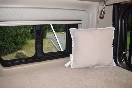 RV rental interior: A cozy bed with pillow, adjustable lamp, and window showing trees, road, and rocks, ideal for travel comfort.