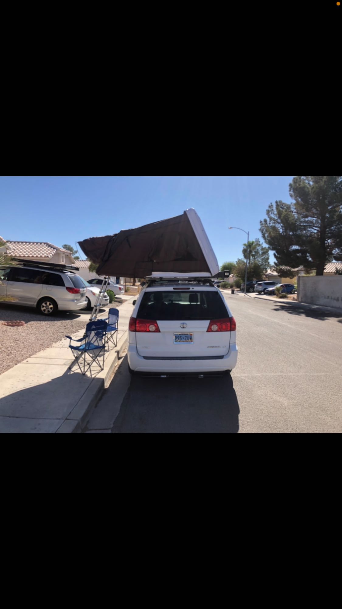  setup for camping by a red rock mountain.|Explore with this compact RV rental: a white Toyota Sienna minivan featuring a deployed rooftop tent for camping.|A white minivan with a deployed rooftop tent — photo 6