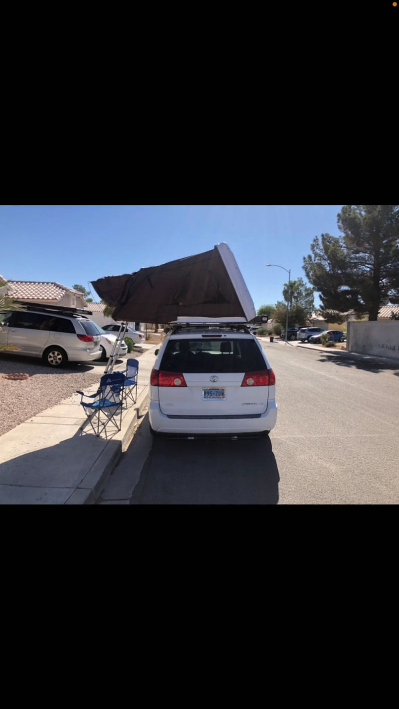  setup for camping by a red rock mountain.|Explore with this compact RV rental: a white Toyota Sienna minivan featuring a deployed rooftop tent for camping.|A white minivan with a deployed rooftop tent — photo 6