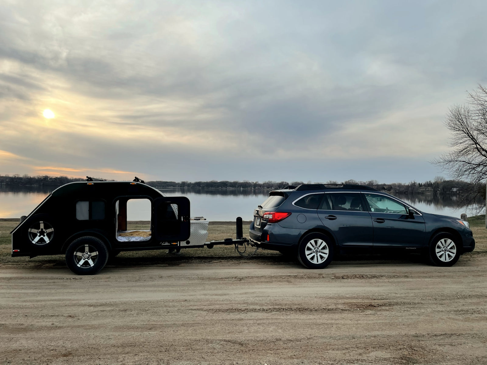 RV rental: Subaru Outback towing a black teardrop camper by a lake. Perfect for serene outdoor travel.|Green teardrop RV rental attached to a car