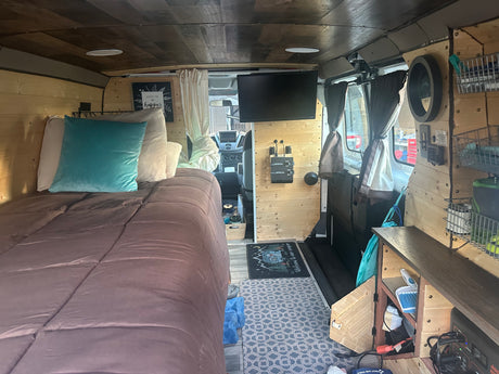 RV rental interior showcasing a comfortable bed, TV, and wooden paneling, offering a cozy travel experience.