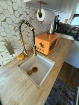 This RV rental boasts a functional tiny kitchen with a stylish brass faucet, hex tiles, wood counter, and orange microwave.