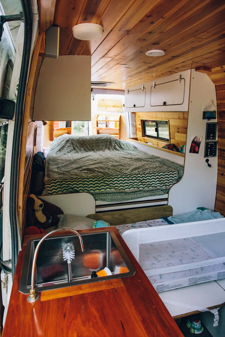 Cozy RV rental interior with a bed, sink, and baby bassinet, surrounded by warm wood paneling. Ideal for family road trips.