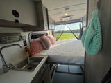 RV rental interior: comfy bed, compact sink, and outdoor view through the back screen.