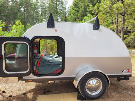 This teardrop trailer rv rental offers a cozy bed in a forest setting, ready for your next outdoor adventure.
