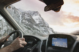 Driving an RV rental through majestic snowy mountains at sunset, hands on the wheel. Dashboard shows 59 mph.