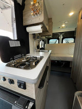 Inside a versatile RV rental: compact kitchen with stove, sink, and spacious rear seating/bed area. Ready for travel.