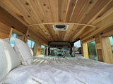 RV rental's inviting interior: A wood-paneled camper van with a large bed, cozy pillows, and window views.