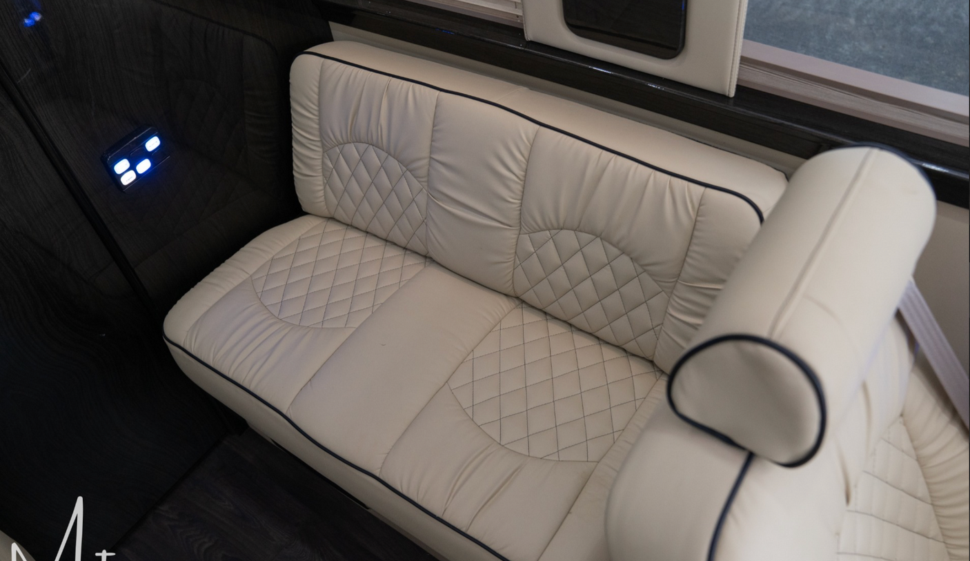 Experience comfort in this RV rental's interior: a cream, quilted bench seat with dark piping, illuminated controls, and wood-grain paneling.