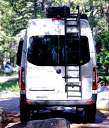 Rear view of a white Winnebago Revel Sprinter van with a ladder and roof rack, perfect for your next rv rental adventure, parked in nature.