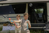 A boy and girl happily blow bubbles beside their RV rental, set up for an outdoor picnic, enjoying family time.