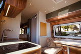 Inside a stylish RV rental: a modern kitchen with induction cooktop, cozy dining area, and bedroom beyond. Ready for adventure!