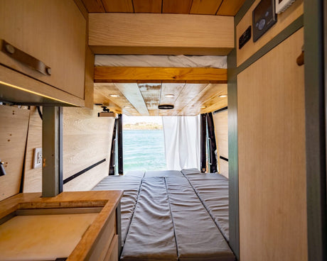 Inside a customized rv rental van: a comfy modular bed with an expansive ocean view out the back.