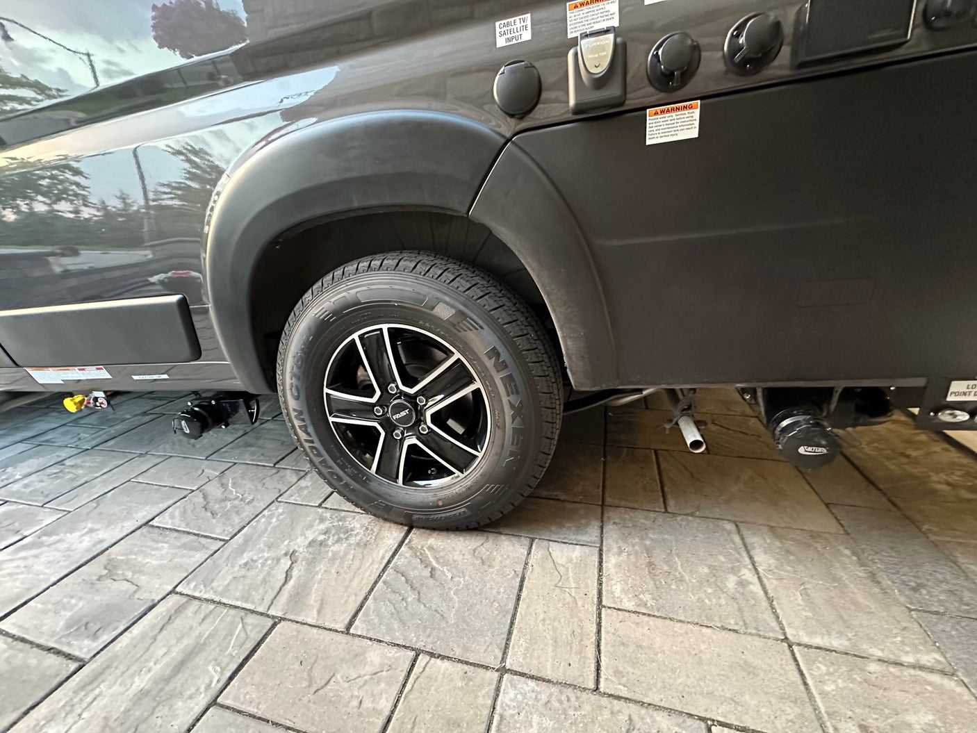 Side view of an RV rental's rear wheel with Nexen tire and Fast wheel, plus essential utility hookups for cable/satellite & power.
